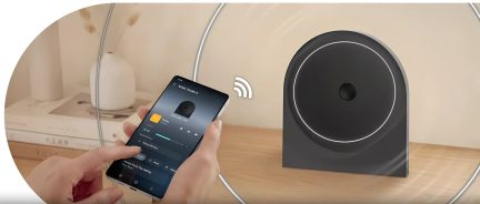 Černý bezdrátový reproduktor s kruhovým designem ovládaný ze smartphonu na dřevěném stole