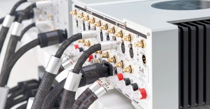 Bagfra af en audioforstærker med guldbelagte RCA-stik, sorte XLR-stik, røde og sorte terminaler, sorte kabelhylstre
