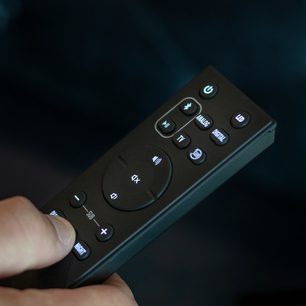 Telecomandă neagră Klipsch Cinema 600 cu butoane iluminate albastru, vedere apropiată frontală pe fundal albastru închis