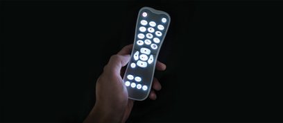 Mando a distancia negro rectangular con botones blancos iluminados sostenido en una mano sobre fondo negro, vista frontal