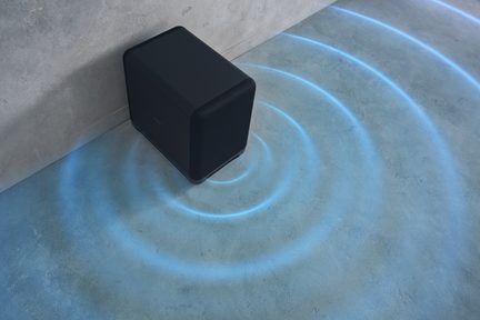 Μαύρο ορθογώνιο μεταλλικό subwoofer με υφασμάτινη μπροστινή γρίλια, στρογγυλεμένες γωνίες, λήψη από ψηλά με μπλε ομόκεντρους κύκλους που ακτινοβολούν στο πάτωμα