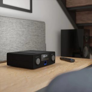 Ampli hi-fi стерео SVS Prime Wireless Pro SoundBase черен, преден изглед на рафта от светло дърво, с черен дистанционен пулт, поставен пред него