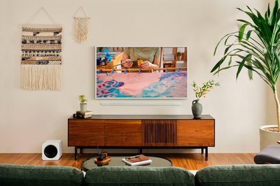 Televisore Samsung TQ65LS03FAU 2025 frontale con cornice bianca, che mostra un'opera colorata, montato a parete sopra un mobile in legno