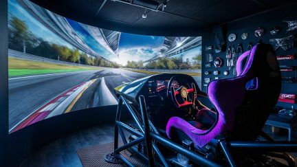 Racingsimulator med lila skålstol, röd ratt och böjd skärm som visar en racerbana