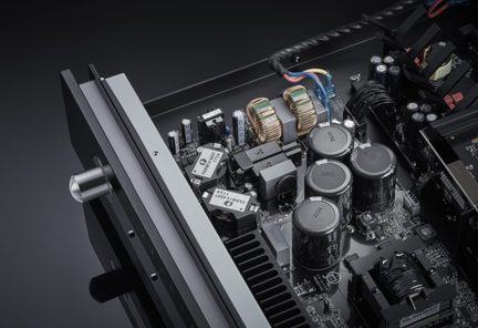 Top-down view of a black integrated amplifier with open cover revealing internal components including capacitors and transformers