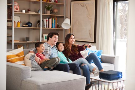 Una famiglia di quattro persone sorridenti seduta su un divano grigio in un soggiorno luminoso e accogliente