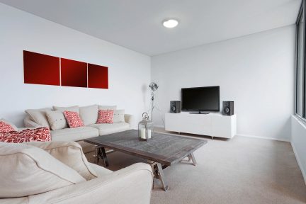 Modern living room with beige sofa, dark wood coffee table, TV, speakers, gray rug, and three red wall panels