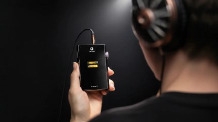 Amplificatore per cuffie portatile Cayin L-Amp II nero tenuto in mano, collegato a cuffie audio