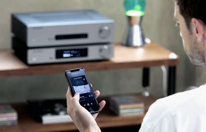 Cambridge Audio CXA61 stereoforstærker i antracitgrå med sølvfinish, nu med smartphone der viser lydgrænsefladen