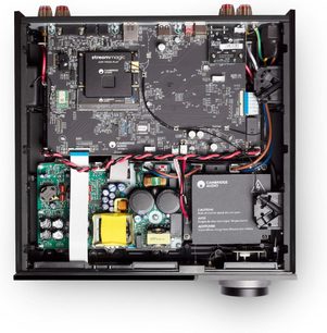 Vista dall’alto dell’interno del Cambridge Audio EVO 150SE, amplificatore hi-fi integrato stereo con chassis in metallo nero che lascia intravedere circuiti stampati neri, trasformatore con nucleo giallo, condensatori cilindrici verdi e neri, cablaggio multicolore e ampia manopola del volume argentata sul frontale