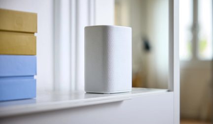 Witte cilindervormige slimme luidspreker op een plank in een lichte, moderne woonkamer