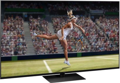 Panasonic TX-75JX940E-fladskærm, der viser en kvindelig tennisspiller i aktion på en grusbane under en kamp