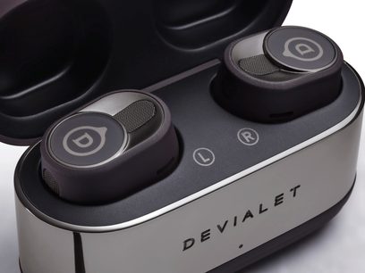 Безжичен слушател Devialet Gemini II в матов черен цвят, изглед отгоре, слушалки в черен овален заряден етикет с лого в сребристо