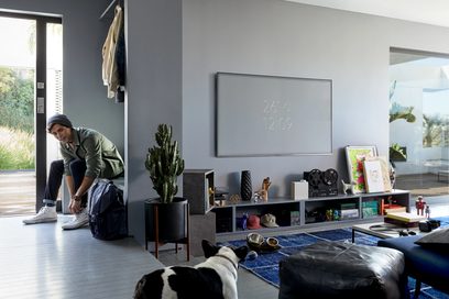 Mand siddende på gulvet i en moderne stue foran en Samsung QE75Q6F 2018 75-tommer tv, der viser klokken 12:09
