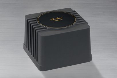 Accuphase P-7500, set fra en vinkel, sort kabinet, rillet overflade, cirkulær top med gyldent logo, metallisk grå baggrund
