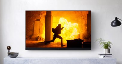 Panasonic TX-65HZ1500E-tv tændt, der viser en mand, der løber i flammer, lampe og grøn plante i nærheden
