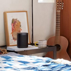 Sonos One (Gen 2) højttaler i mat sort, akustisk guitar, indrammet abstrakt tegning, krus, seng med blåt bølgemønstret tæppe