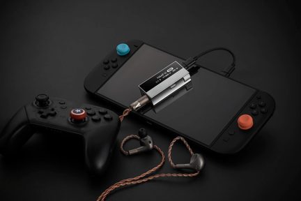 Сріблястий аудіоадаптер USB-C, під’єднаний до Nintendo Switch, з чорною манеткою та дротовими внутрішньоканальними навушниками