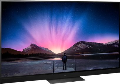 Panasonic TX-77LZ2000E-tv, der viser et lyserødt nordlys over sneklædte bjerge, med en person stående på en bådebro i forgrunden af en frossen sø