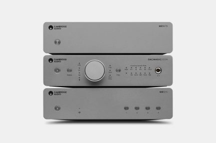 Vista frontale di tre dispositivi audio hi-fi impilati, frontali rettangolari in alluminio grigio opaco con pulsanti circolari di accensione a sinistra, ampia manopola centrale e indicatori LED sull’unità intermedia, presa per cuffie a destra e quattro piccoli pulsanti allineati sull’unità inferiore
