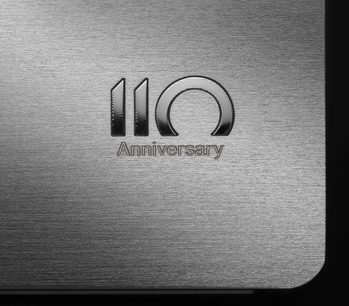 Logoet "110 Anniversary" indgraveret på en rektangulær børstet metaloverflade, tæt centreret billede