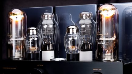 Nærbillede, frontvisning af en sort rørforstærker med flere cylindriske elektronrør i gennemsigtigt glas med metalbaser, hvoraf nogle har orangeglødende filamenter