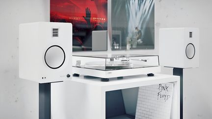 Instalație audio albă compusă dintr-un pickup cu capac transparent din plastic și două boxe rectangulare albe cu finisaj mat, fiecare având difuzor circular negru, vedere din unghi de trei sferturi