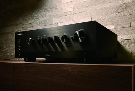 amplificator hi-fi stereo Yamaha negru cu fațadă din aluminiu periat, buton mare de volum și selectoare pe mobilier din lemn