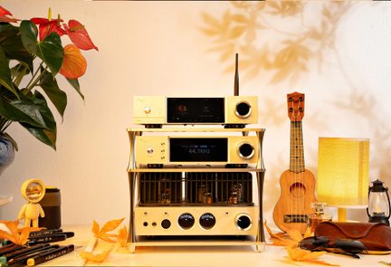 Champagne-colored modular hi-fi audio system in brushed metal, consisting of three rectangular units stacked on an open frame, each featuring a central black display and large circular buttons, front view