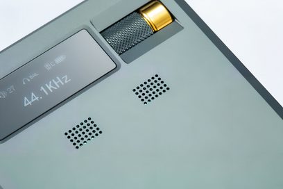 Bærbar lydkonverter Cayin RU9 i mat grøn aluminium, tæt på i trekvartsvisning, der afslører monokrom skærm, to perforerede gitter og delvist indbygget gylden rillet volumenknap