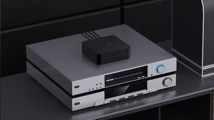 Un involucro nero con cavi posato su due dispositivi elettronici argentati impilati, pulsanti e display visibili, sfondo nero testurizzato