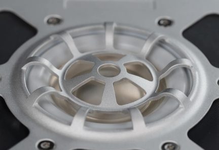 Oblique close-up of a silver aluminum spoked circular grille above a translucent element, with visible screws