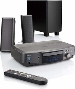 Denon S-102 hjemmebiograf-system bestående af en CD-afspiller med blå LCD-skærm, to sorte højttalere og en fjernbetjening, set forfra på hvid baggrund
