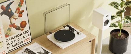 Hvid vinylpladespiller med sort pladetallerken og transparent låg, placeret på et træmøbel, set ovenfra