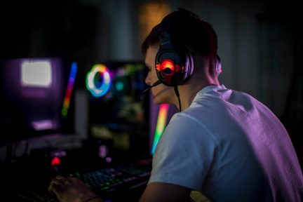 Čierna herná náhlavná súprava s mikrofónom a červeným osvetlením, nosená zozadu pred RGB PC zostavou pri slabom osvetlení