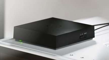 Černý obdélníkový TV box v tříčtvrtečním pohledu se zelenou kontrolkou a tlačítkem reset na přední straně