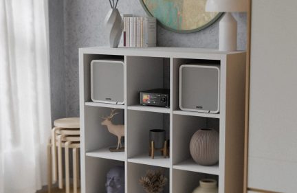 Schwarze Hi-Fi-Anlage mit Farbdisplay und zwei quadratischen weißen Lautsprechern, in einem Würfelregal aufgestellt