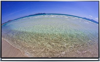 Bred strand med lys, fin sand omkranset af et turkisfarvet hav, vidvinkel luftfoto i froskeperspektiv under en klar, blå himmel