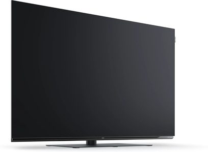 Loewe We. SEE 65 OLED dc black flat-screen television with thin bezel and central stand, front view at a slight angle