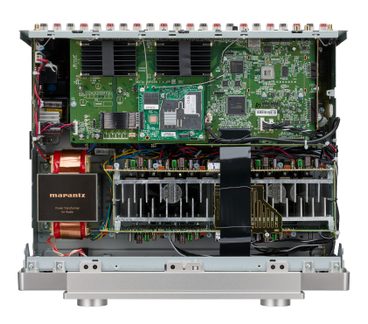 Binnenkant van een grijze metalen audioversterker, groene printplaten, koperen Marantz-transformator, grote koellichamen