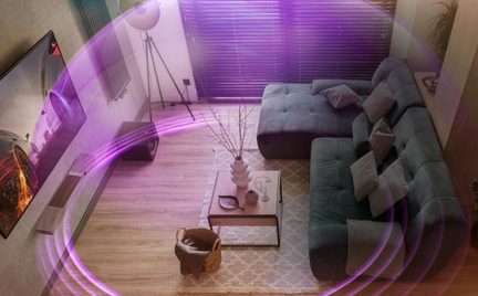 surround soundbar v moderním obývacím pokoji, fialové světelné efekty ilustrující 3D šíření zvuku kolem pohovky