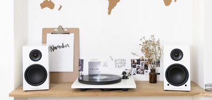 Pladespiller, to højttalere, kalender, billeder og vase med tørrede blomster placeret på et lyst trænøbel