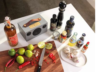 Enceinte Audio Pro ADDON C3 gris, limes, piments rouges, ail, couteaux, bouteilles d'alcool et de jus sur planche en bois