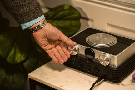 sølvfarvet iFi hi-fi-lydforstærker med store volumenknapper, mandlig hånd der justerer det forreste hjul