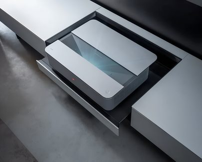 Hvidt ultrakortkast-laserprojektor med minimalistisk, rektangulært design, integreret i gråt tv-møbel