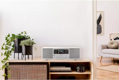 Sonoro Primus glossy white - silver tabletop radio, front view, placed on a light wood cabinet with green plants