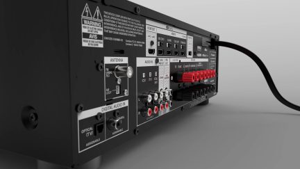 Zadní část černého audio-videoreceiveru s mnoha konektory a označenými porty, do kterého je zapojen červený kabel