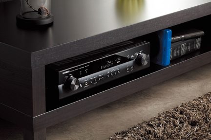 Černý audio přijímač v tmavém dřevěném nábytku, detailní pohled zepředu