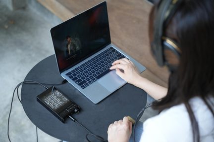 Fekete Questyle hordozható USB DAC fejhallgató-erősítő laptop és hi-fi fejhallgató mellett elhelyezve