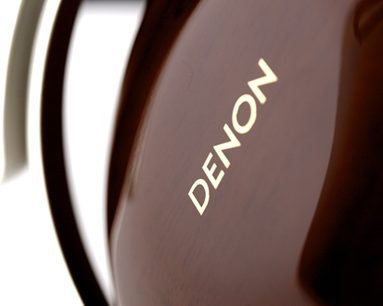 Close-up van de Denon AH-D7000 hoofdtelefoon, zijaanzicht, gouden "DENON"-logo op glanzende donkerbruine behuizing